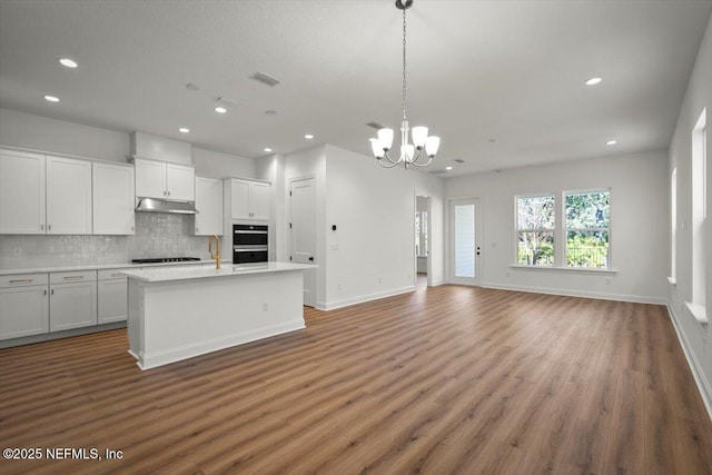 kitchen featuring backsplash, hanging light fixtures, a center island with sink, and white cabinets