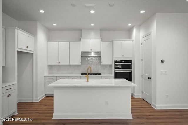 kitchen with white cabinetry, a kitchen island with sink, light stone counters, and black appliances