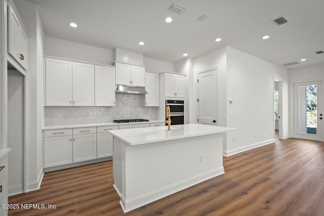 kitchen featuring decorative backsplash, black appliances, an island with sink, and white cabinets