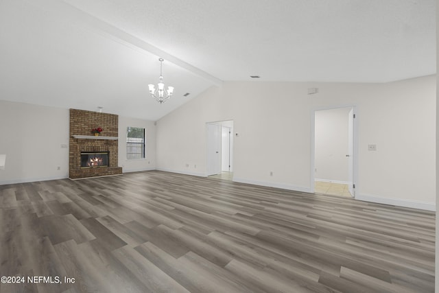 unfurnished living room featuring wood-type flooring, lofted ceiling with beams, a textured ceiling, a brick fireplace, and a notable chandelier