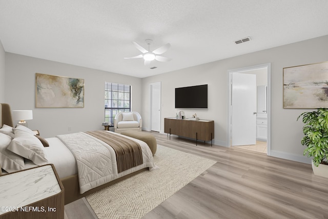 bedroom featuring light wood-type flooring, connected bathroom, a textured ceiling, and ceiling fan