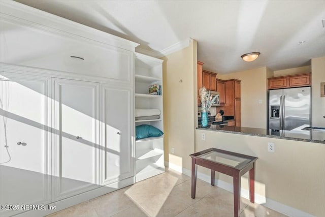 kitchen featuring light tile patterned flooring, sink, dark stone countertops, stainless steel fridge, and ornamental molding