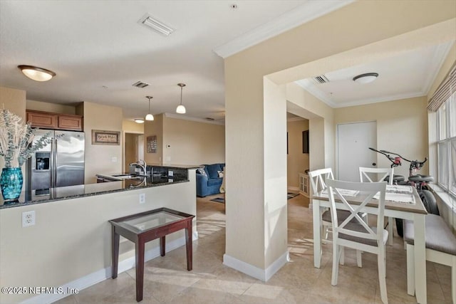 kitchen featuring decorative light fixtures, sink, crown molding, dark stone counters, and stainless steel refrigerator with ice dispenser