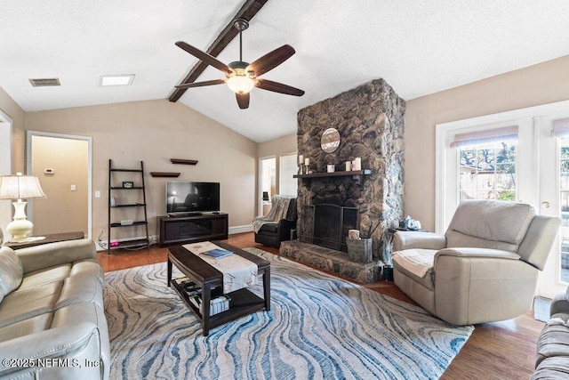 living room featuring lofted ceiling with beams, a stone fireplace, hardwood / wood-style flooring, and ceiling fan