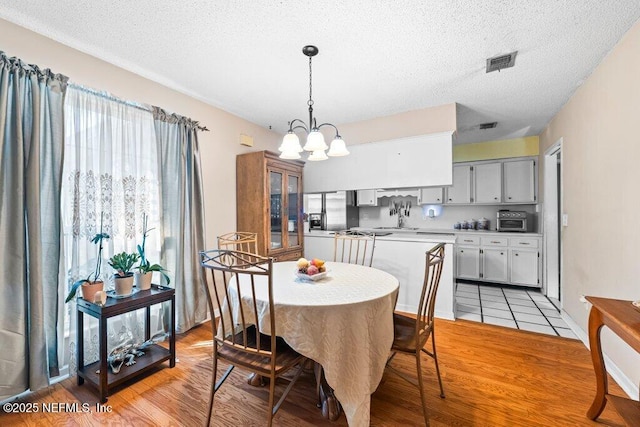 dining space with a notable chandelier, light hardwood / wood-style floors, and a textured ceiling