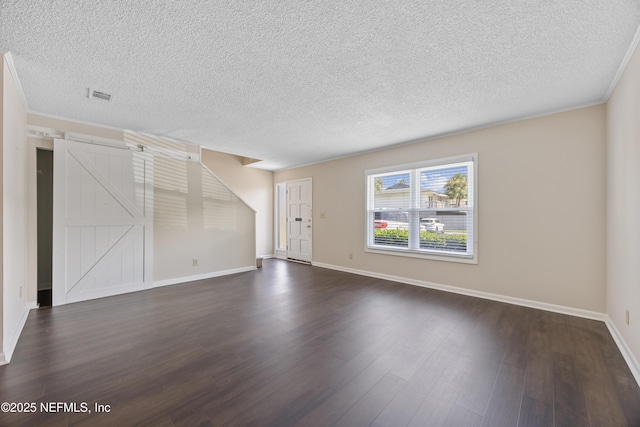 unfurnished living room with ornamental molding, a barn door, dark hardwood / wood-style floors, and a textured ceiling