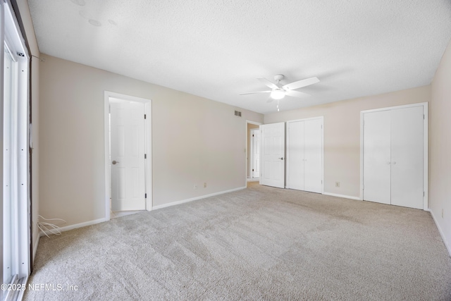 unfurnished bedroom with light carpet, ceiling fan, a textured ceiling, and multiple closets