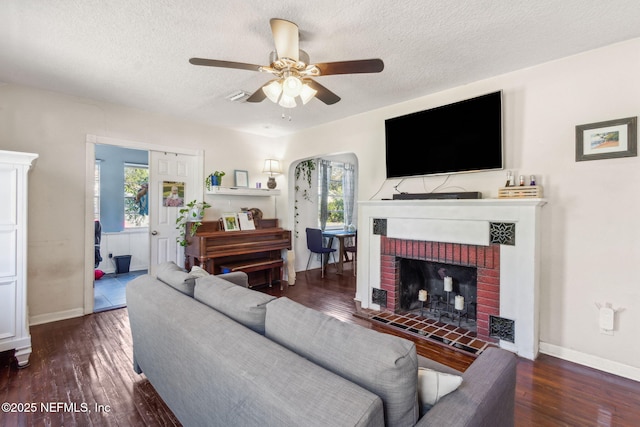 living room featuring a fireplace, dark wood-type flooring, a textured ceiling, and ceiling fan