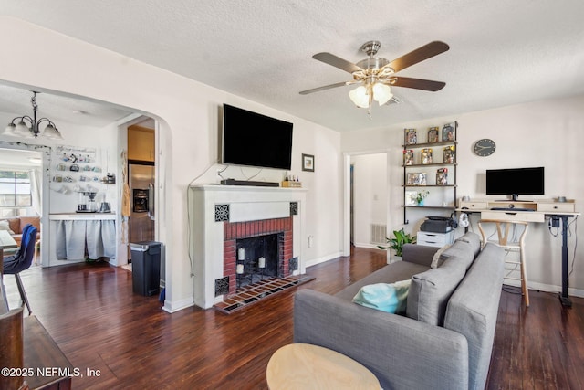 living room with dark hardwood / wood-style flooring, ceiling fan with notable chandelier, a fireplace, and a textured ceiling