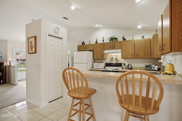 kitchen featuring a kitchen bar, vaulted ceiling, light tile patterned floors, kitchen peninsula, and white appliances