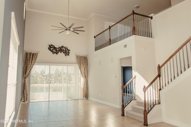 unfurnished living room with a high ceiling, crown molding, light tile patterned flooring, and ceiling fan