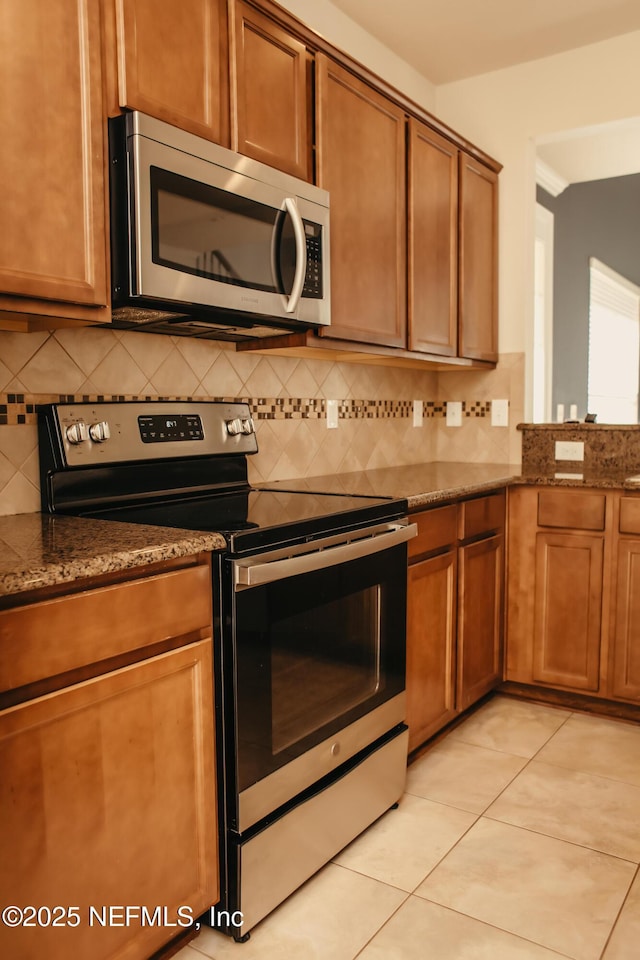 kitchen with appliances with stainless steel finishes, light tile patterned floors, decorative backsplash, and dark stone counters