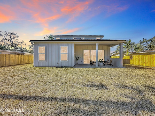 back house at dusk featuring a lawn and a patio area