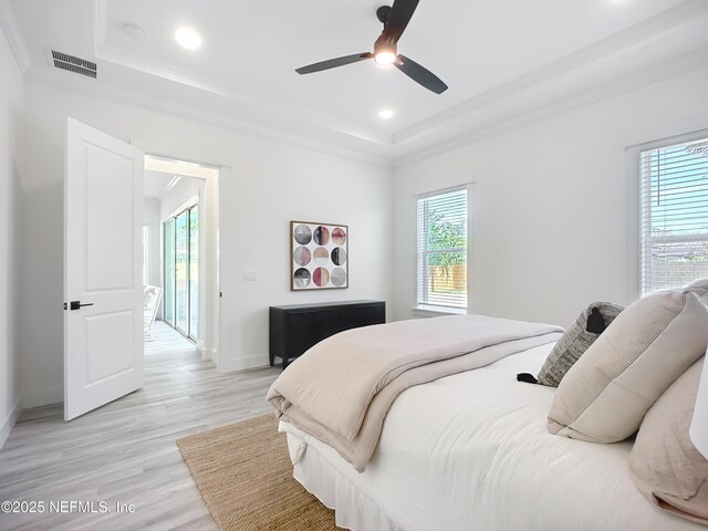 bedroom with ceiling fan, a tray ceiling, and light hardwood / wood-style floors