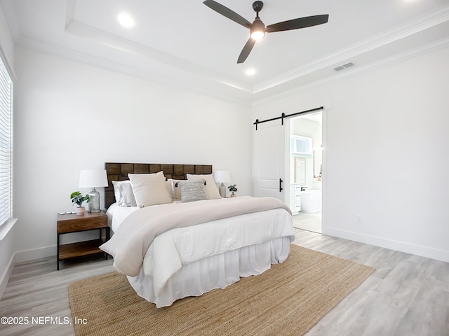 bedroom featuring ensuite bathroom, ornamental molding, light hardwood / wood-style floors, a raised ceiling, and a barn door