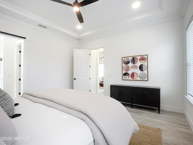 bedroom with ornamental molding, ceiling fan, a tray ceiling, a barn door, and light hardwood / wood-style flooring