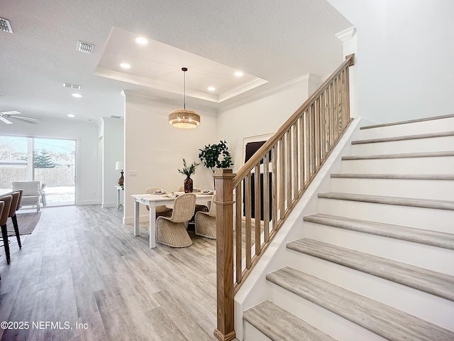 staircase featuring crown molding, ceiling fan, hardwood / wood-style floors, a tray ceiling, and a textured ceiling