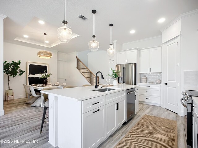 kitchen featuring decorative light fixtures, stainless steel appliances, white cabinets, and a center island with sink