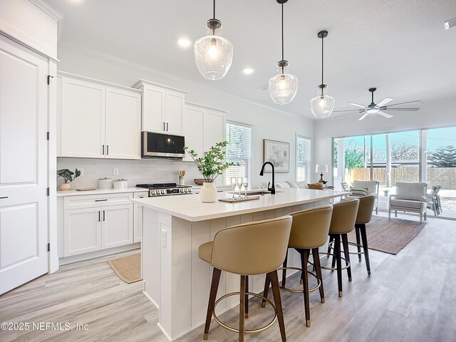 kitchen featuring a kitchen island with sink, decorative light fixtures, and white cabinetry