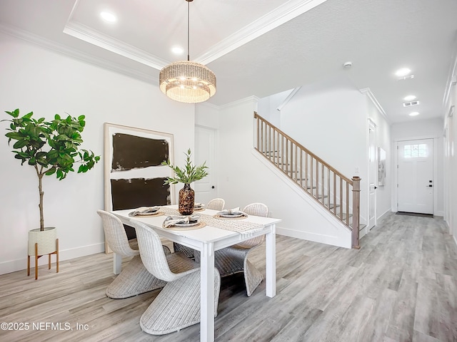 dining area featuring ornamental molding, a tray ceiling, a chandelier, and light hardwood / wood-style flooring