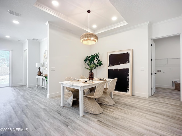 dining space featuring a raised ceiling, crown molding, and light hardwood / wood-style floors