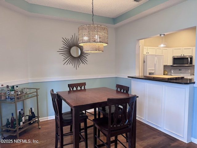 dining area featuring dark wood-type flooring, a textured ceiling, and a tray ceiling