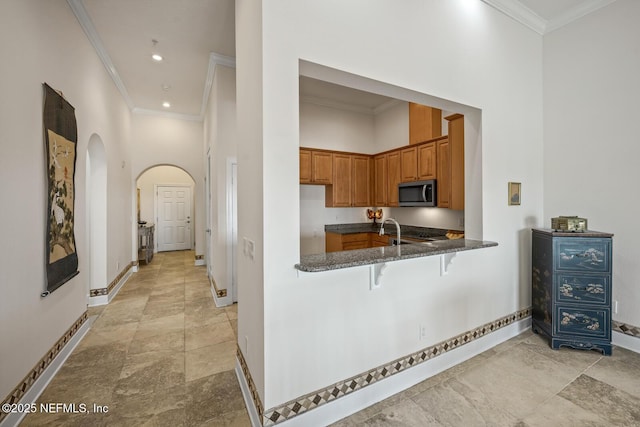 kitchen with crown molding, dark stone counters, kitchen peninsula, and a high ceiling