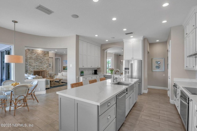 kitchen with pendant lighting, white cabinetry, sink, stainless steel appliances, and a center island with sink