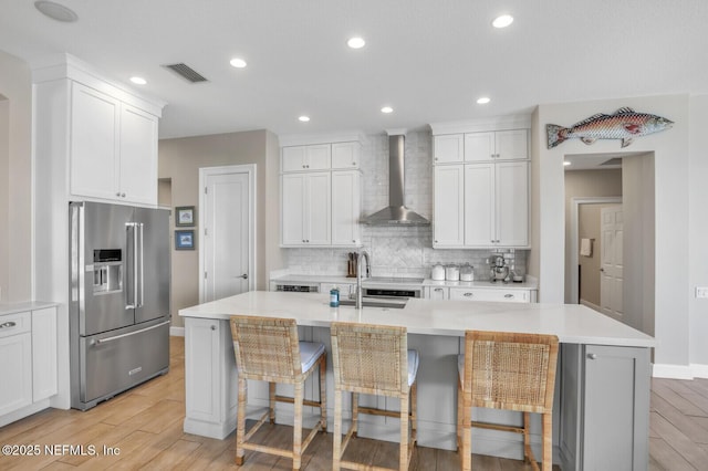 kitchen with wall chimney exhaust hood, high end refrigerator, a breakfast bar, and a kitchen island with sink