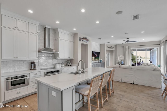 kitchen featuring wall chimney exhaust hood, a kitchen bar, sink, a center island with sink, and white cabinets