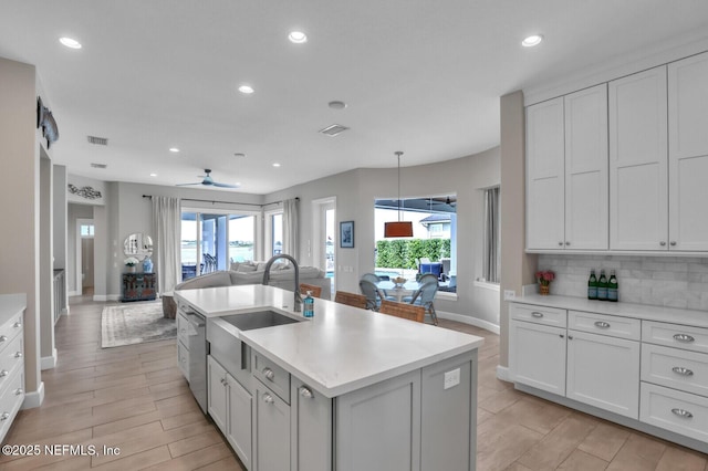 kitchen with tasteful backsplash, white cabinetry, sink, hanging light fixtures, and a kitchen island with sink