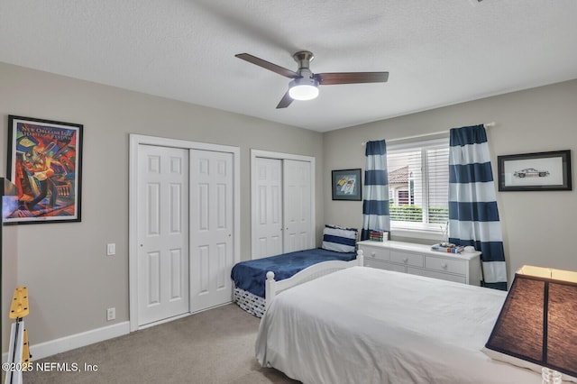 carpeted bedroom with two closets, a textured ceiling, and ceiling fan