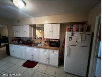 kitchen featuring white refrigerator, white cabinetry, sink, and light tile patterned floors