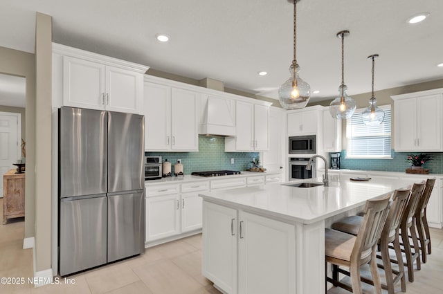 kitchen featuring premium range hood, sink, hanging light fixtures, stainless steel appliances, and a center island with sink