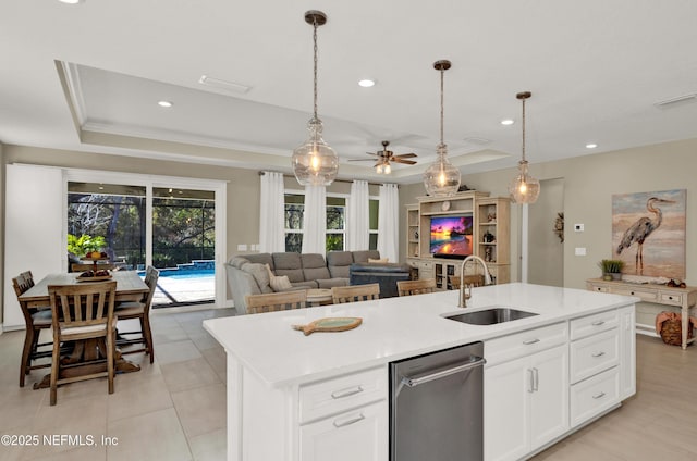 kitchen with sink, dishwasher, white cabinetry, a tray ceiling, and a center island with sink