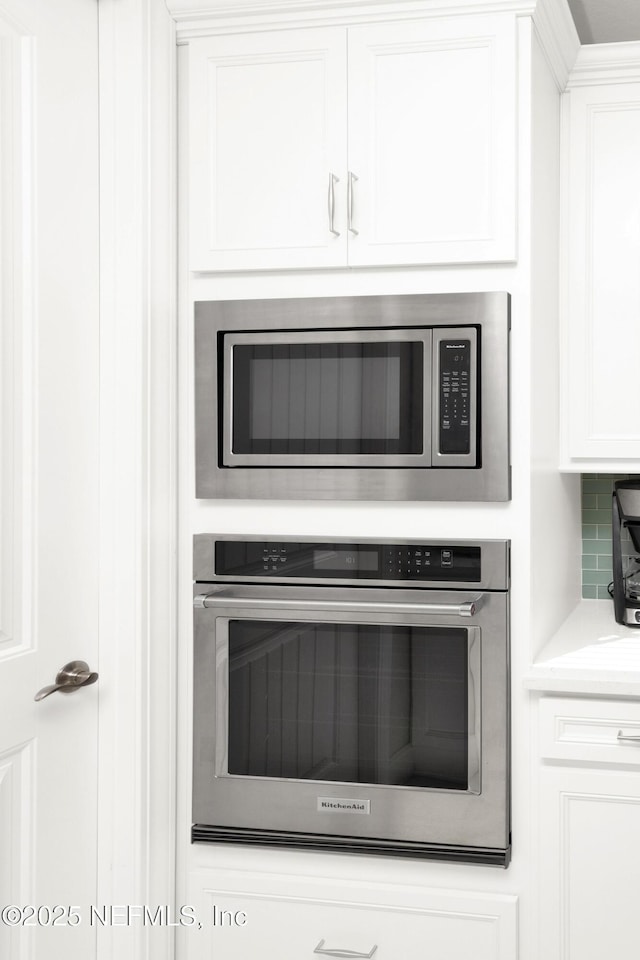 room details featuring appliances with stainless steel finishes, white cabinets, and decorative backsplash