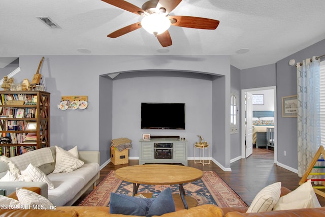 living room featuring dark hardwood / wood-style flooring, ceiling fan, and a textured ceiling