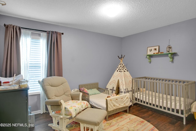 bedroom featuring dark hardwood / wood-style flooring, multiple windows, a nursery area, and a textured ceiling