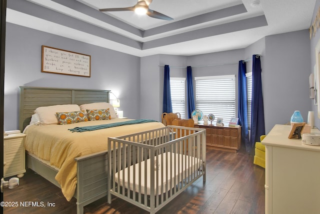 bedroom with a tray ceiling, dark hardwood / wood-style floors, and ceiling fan