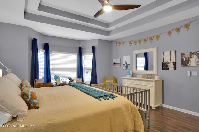 bedroom with dark wood-type flooring, ceiling fan, and a tray ceiling