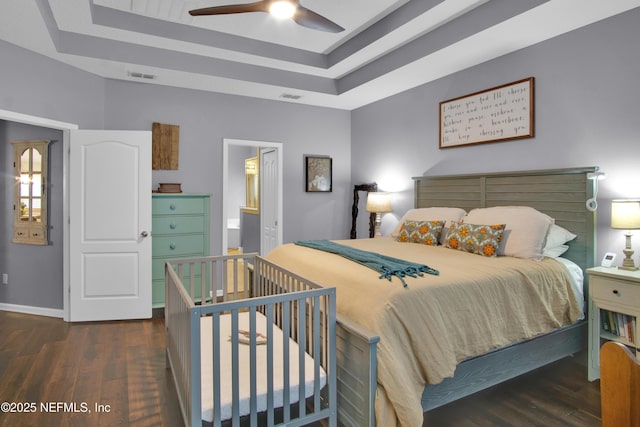 bedroom with dark hardwood / wood-style floors, ceiling fan, a tray ceiling, and ensuite bath