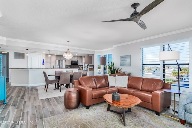 living room featuring ornamental molding, ceiling fan with notable chandelier, a textured ceiling, and light hardwood / wood-style flooring