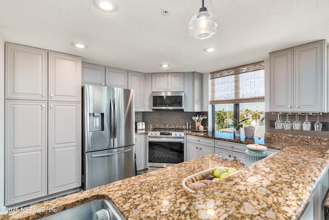 kitchen with pendant lighting, appliances with stainless steel finishes, gray cabinets, and dark stone counters