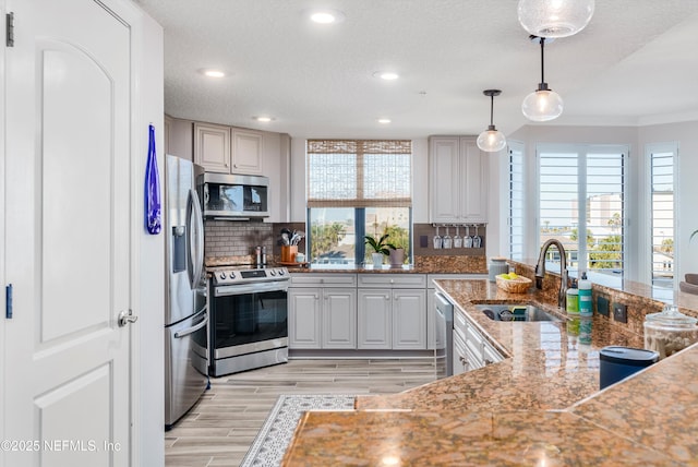 kitchen with appliances with stainless steel finishes, tasteful backsplash, sink, hanging light fixtures, and a healthy amount of sunlight