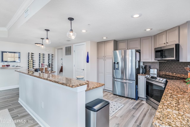 kitchen with gray cabinetry, light stone counters, hanging light fixtures, appliances with stainless steel finishes, and backsplash