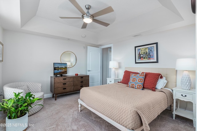 bedroom featuring ceiling fan, a raised ceiling, and light carpet