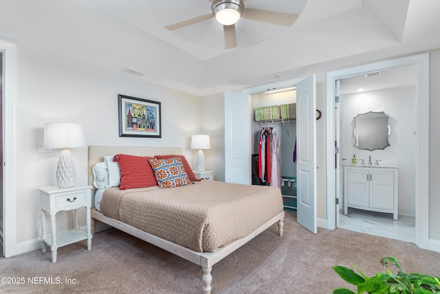 bedroom featuring connected bathroom, a spacious closet, light carpet, a raised ceiling, and a closet