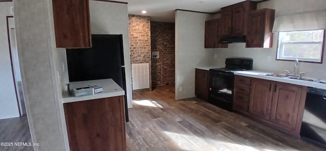 kitchen featuring sink, light hardwood / wood-style flooring, brick wall, range hood, and black appliances