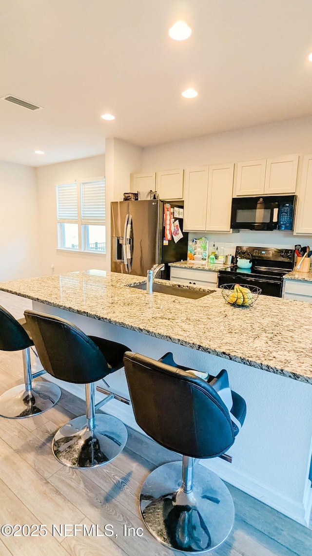 kitchen with light stone countertops, black appliances, and white cabinets