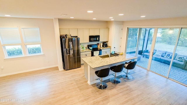 kitchen featuring a breakfast bar, light stone counters, black appliances, an island with sink, and white cabinets